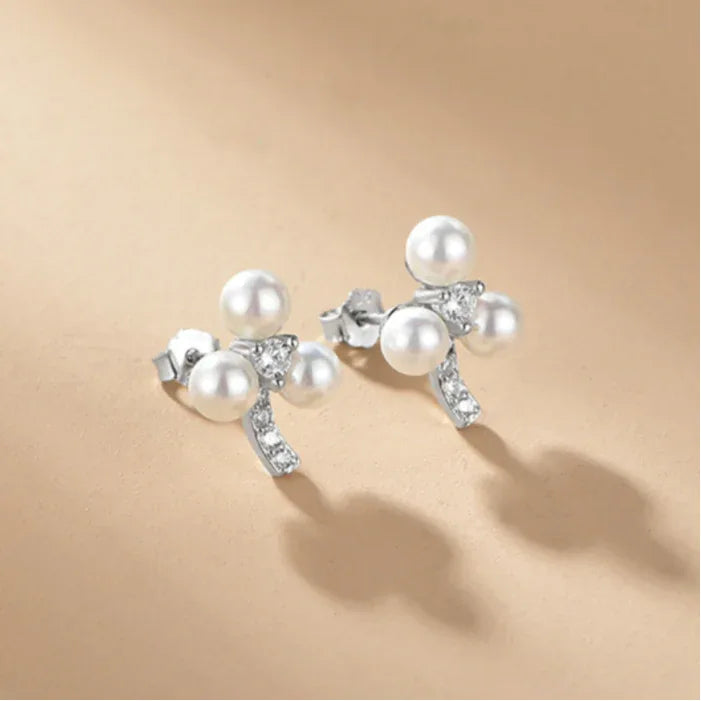 Three-Pearl Bow Stud Earrings in Platinum-Plated S925 Silver — front pair on a beige surface