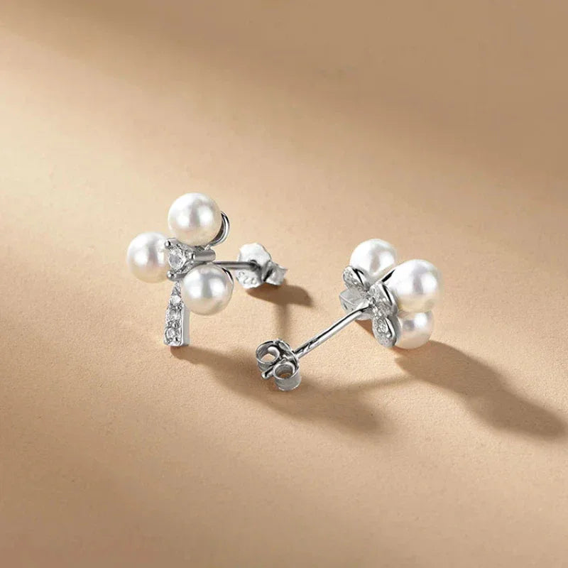 Three-Pearl Bow Stud Earrings in Platinum-Plated S925 Silver — alternate rear-angled pair on a beige surface