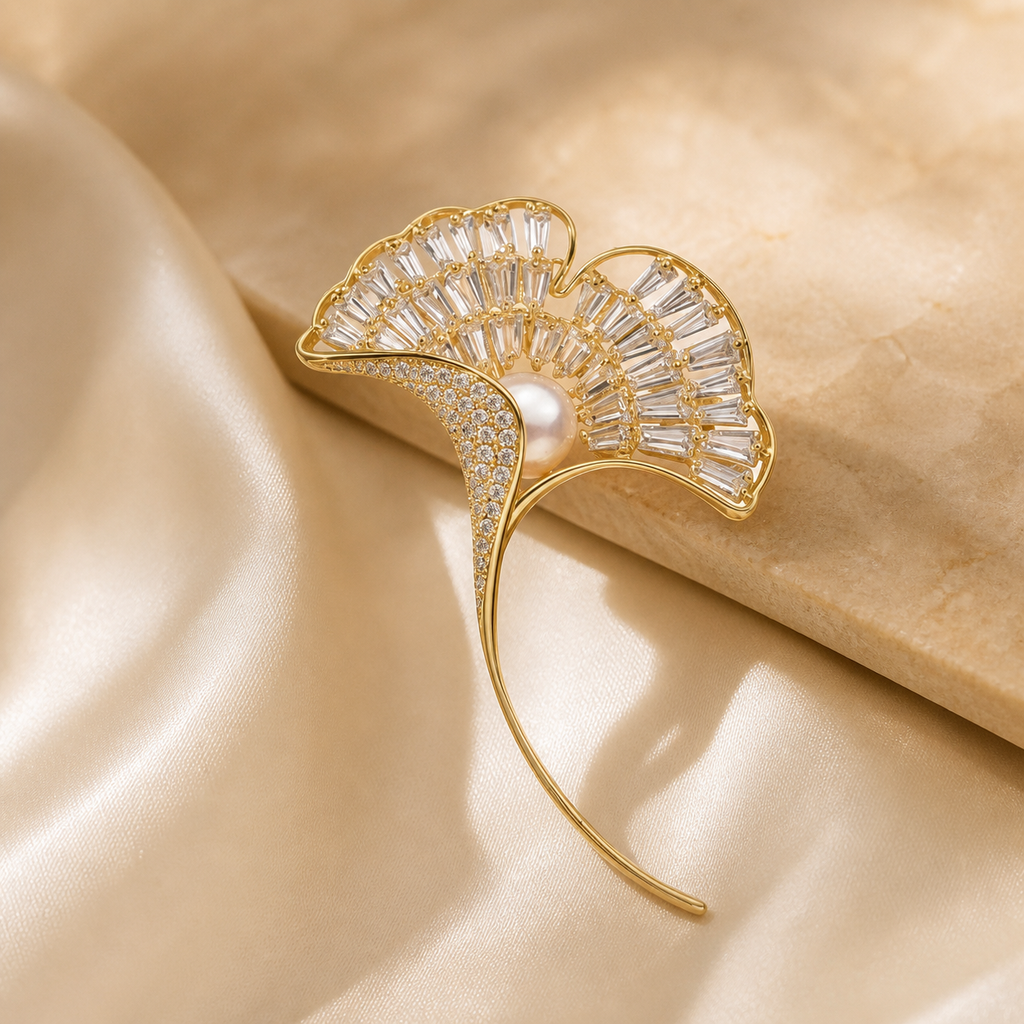 Gold-tone ginkgo leaf brooch with pearl and clear baguette accents on ivory silk