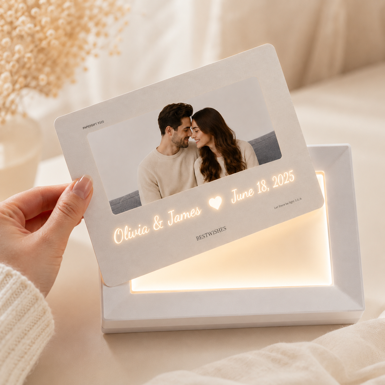 Hand holding personalized hidden message film card above illuminated white LED light frame base showing warm golden glow