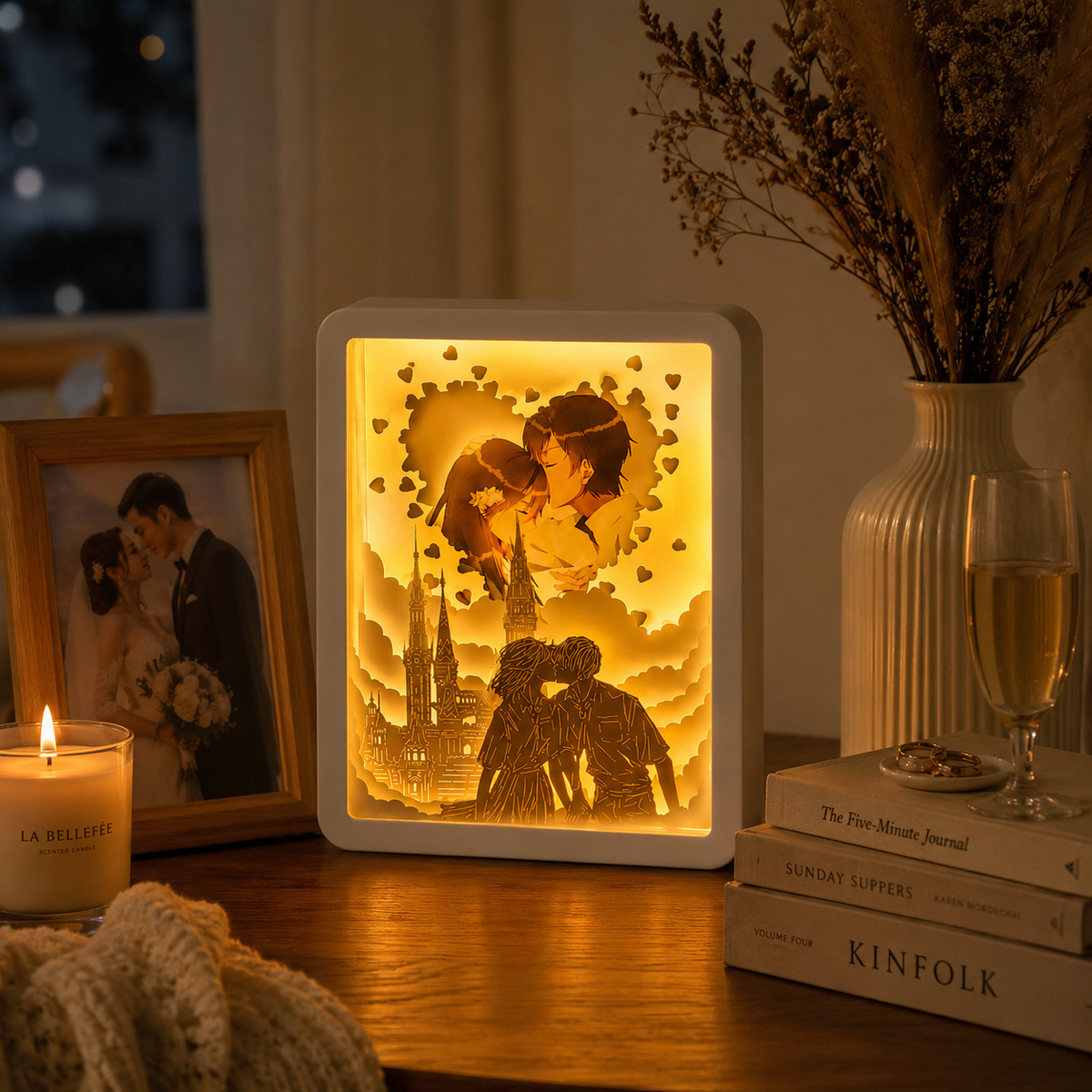 Personalized paper cut light box displayed on a walnut shelf beside stacked books champagne glass and ceramic vase