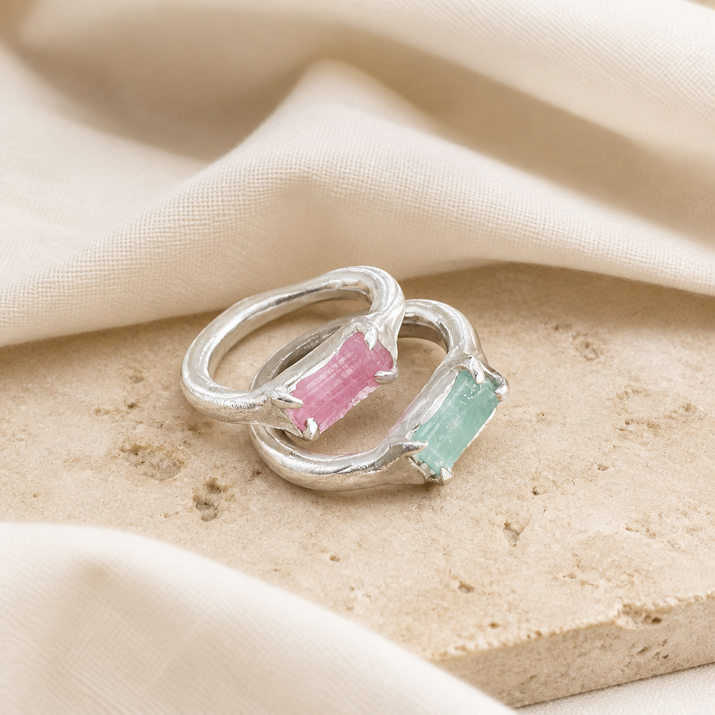 Pair of silver-tone rings with rough-cut pink and aqua rectangular stones on beige