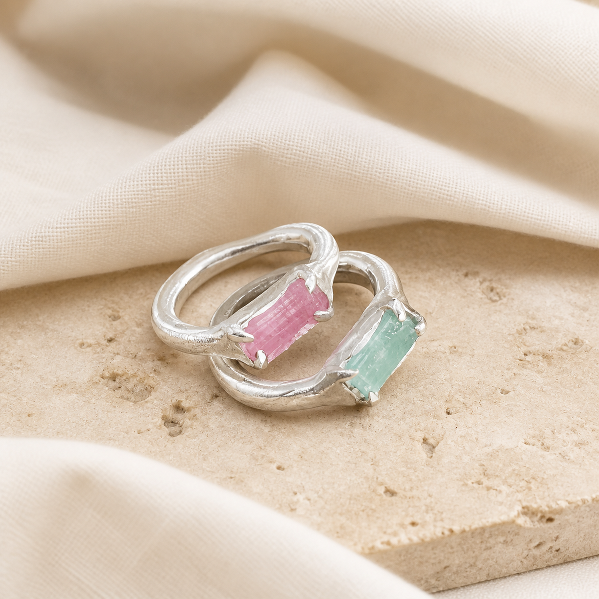 Pair of silver-tone rings with rough-cut pink and aqua rectangular stones on beige