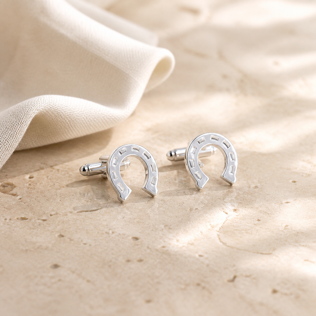 Pair of polished horseshoe cufflinks with rectangular details displayed on warm beige stone