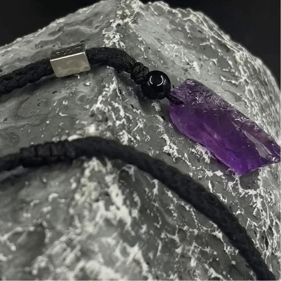 raw amethyst crystal cord necklace crystal point and braided cord on a textured surface