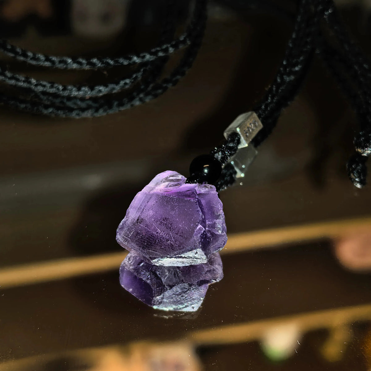 raw amethyst crystal cord necklace crystal point close-up on a dark surface