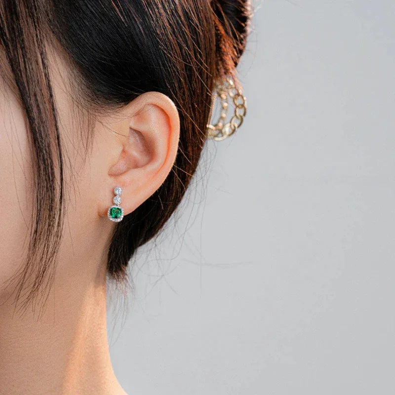 Rectangular Emerald Drop Earrings worn on the ear in a close-up