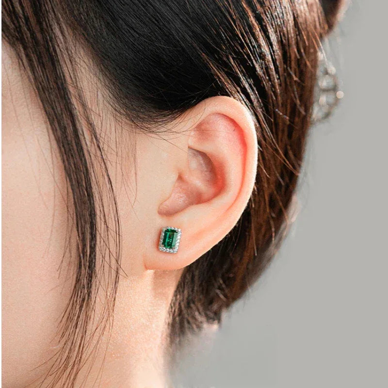 Rectangular Emerald Halo Stud Earrings worn on the ear in a close-up