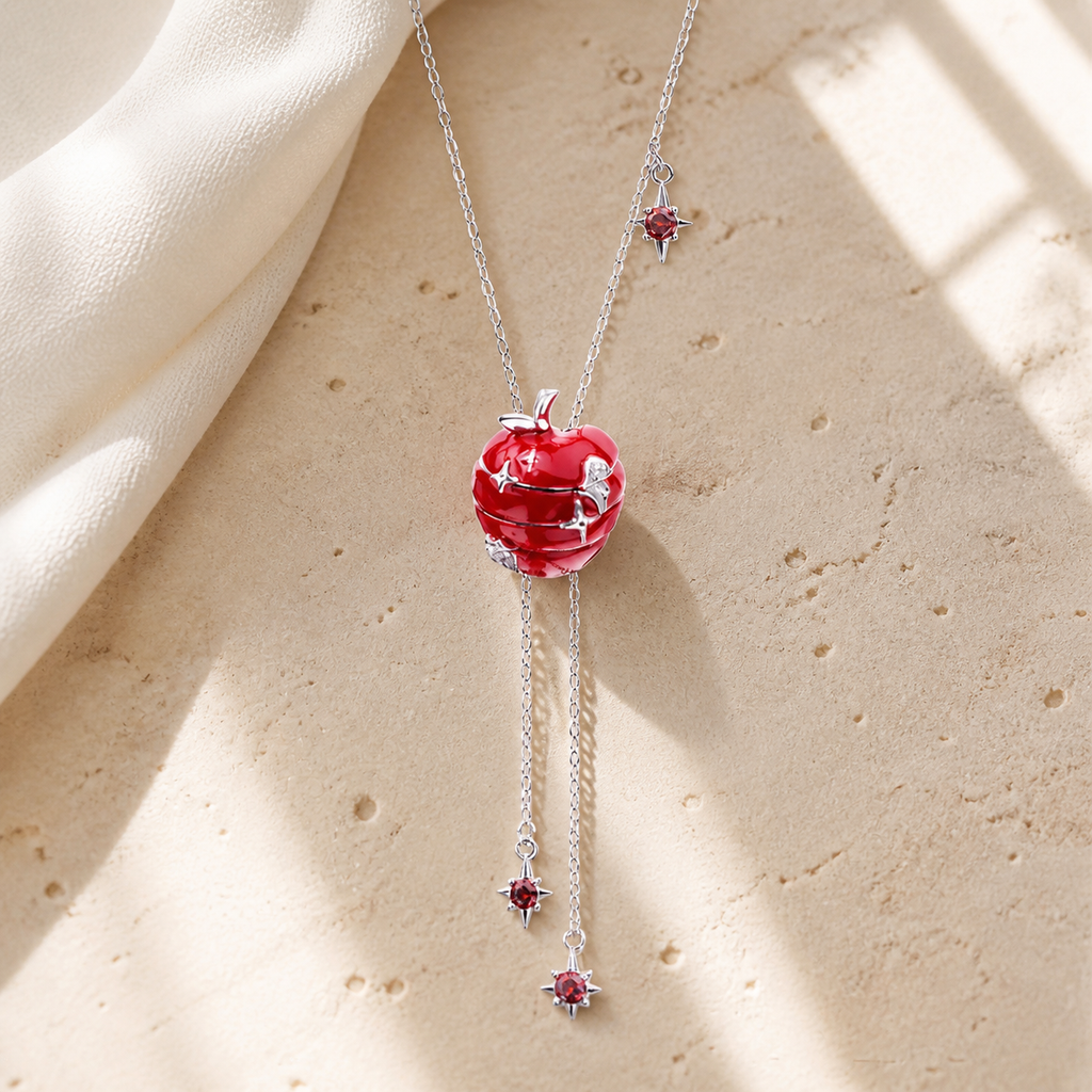 Silver lariat necklace with a red apple pendant and two dangling red star accents on beige stone