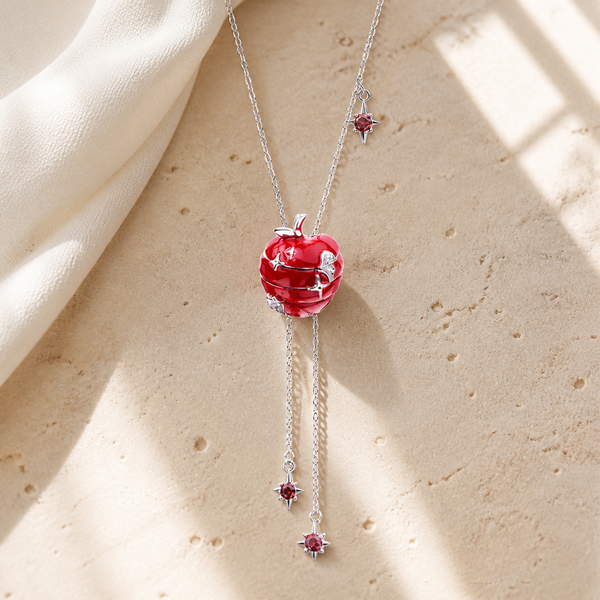 Silver lariat necklace with a red apple pendant and two dangling red star accents on beige stone