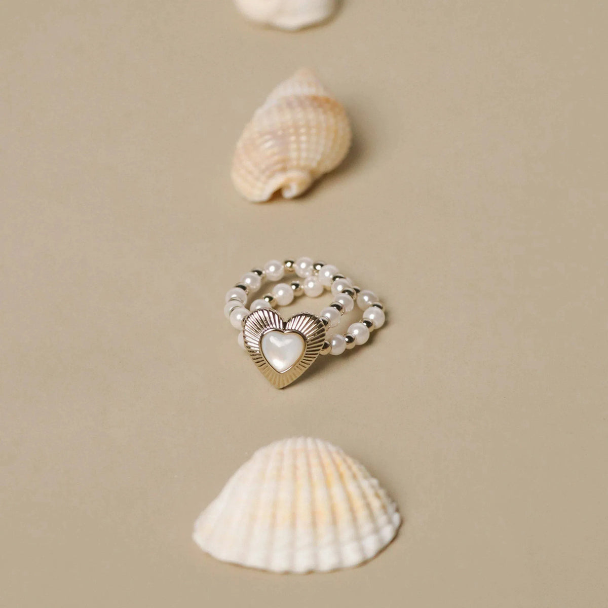 Triple-Row Pearl Heart Stretch Ring — ring displayed with seashells on a pale surface