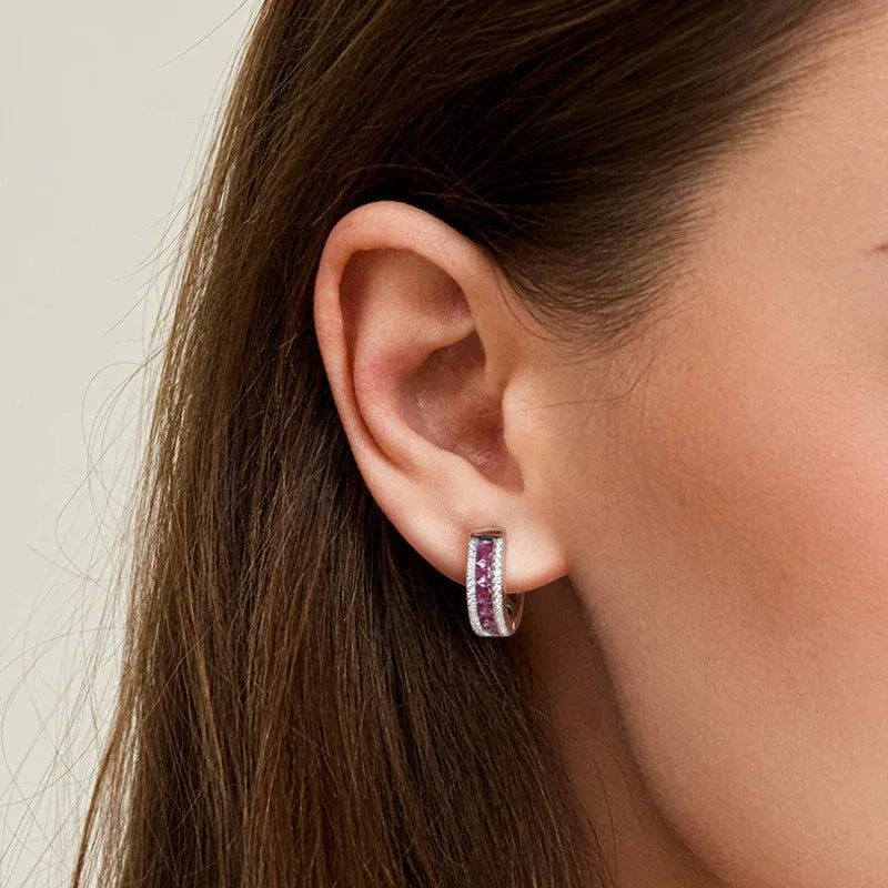 Rose-Purple Garnet Huggie Hoop Earrings worn on the hand in a close-up
