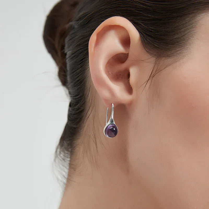 round amethyst drop earrings worn on the ear in a close-up