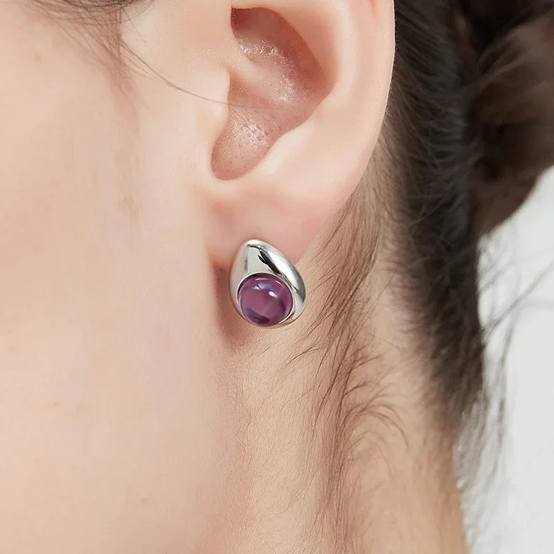 round amethyst stud earrings worn on the ear in a close-up