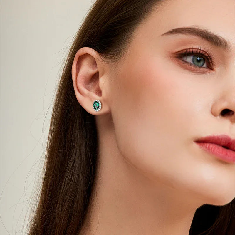 Round Emerald Halo Stud Earrings worn on the ear in a close-up
