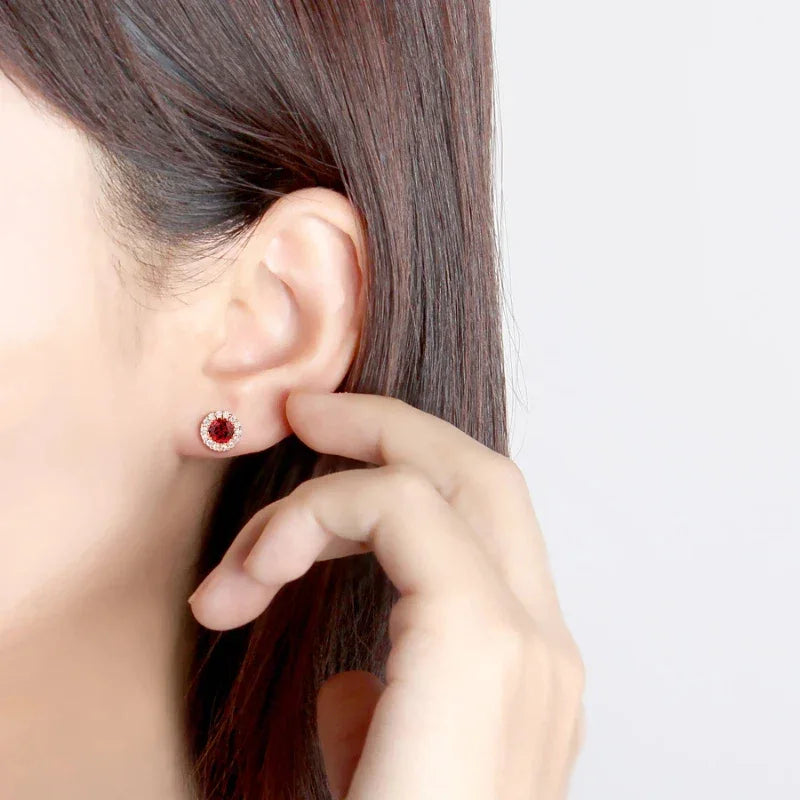 Round Garnet Halo Stud Earrings worn on the hand in a close-up