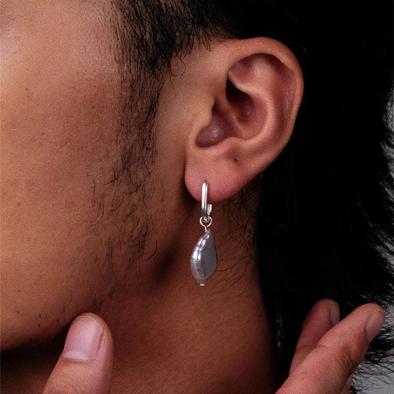 Irregular Pearl Drop Huggie Earrings — left-ear worn close-up with a fingertip indicating scale