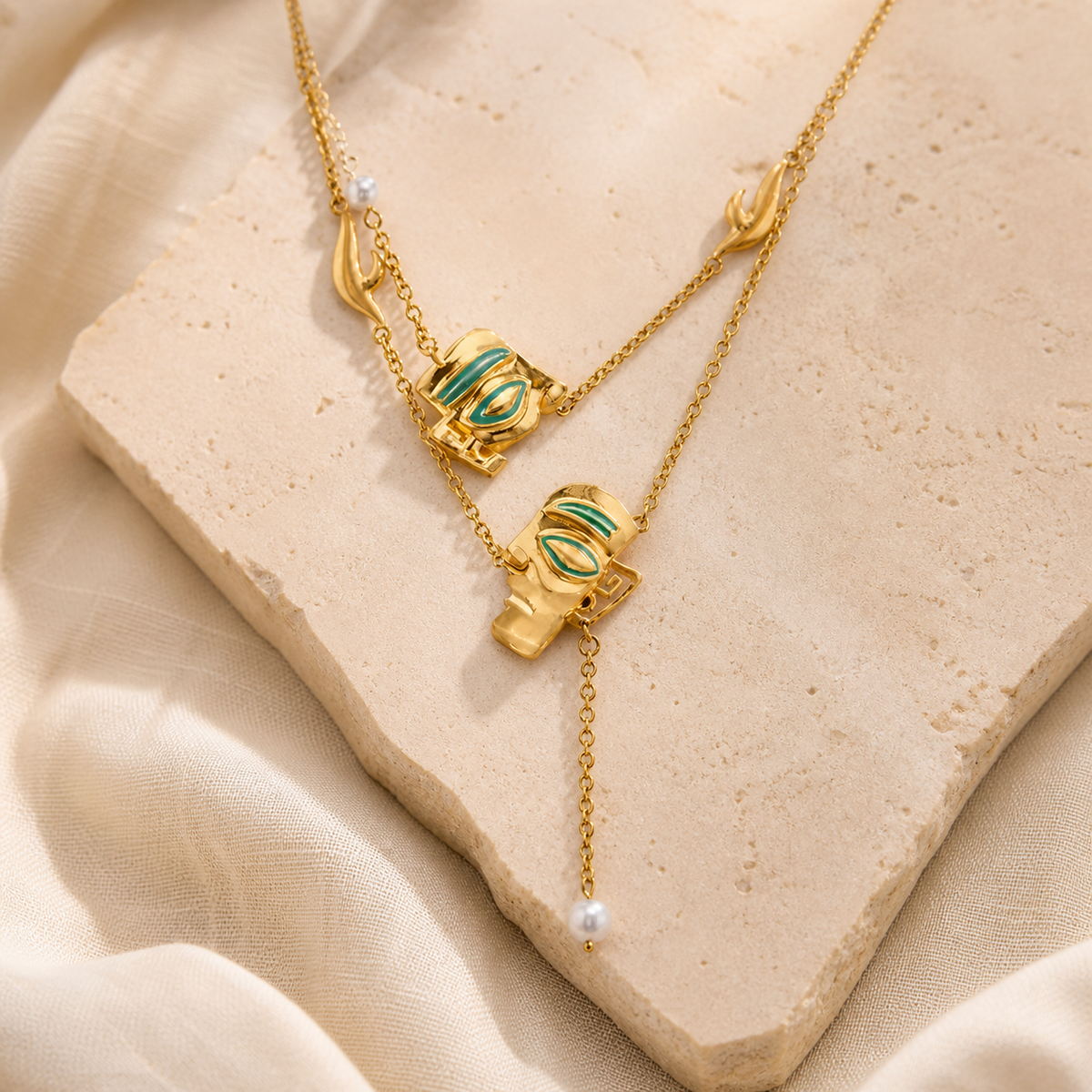 Gold-tone layered necklace with green enamel Sanxingdui motifs and a white bead drop on beige stone
