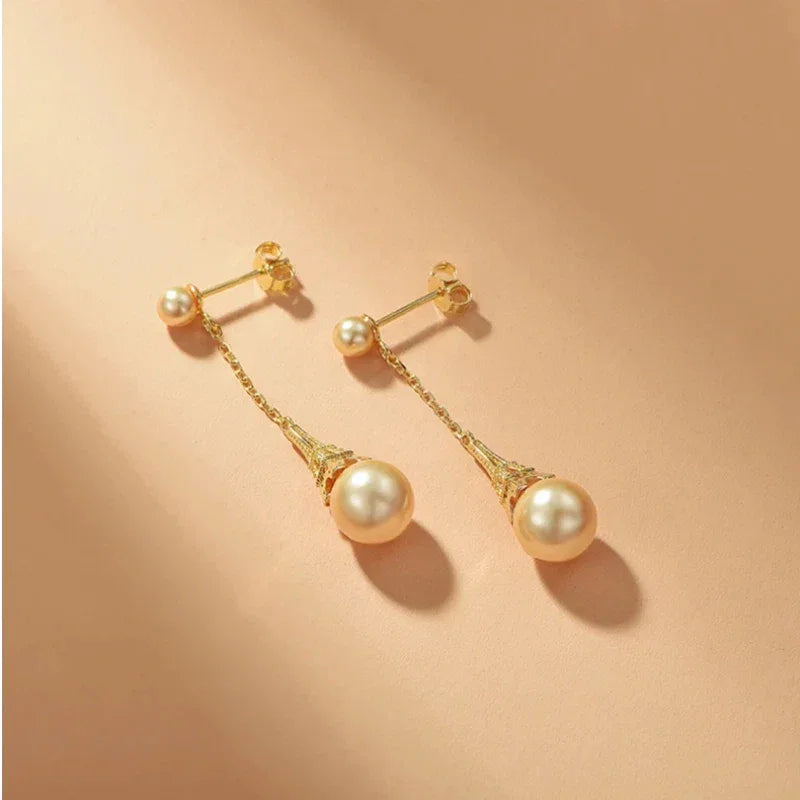 Shell Pearl Eiffel Tower Drop Earrings — gold-tone pair laid on a beige surface showing the post backs
