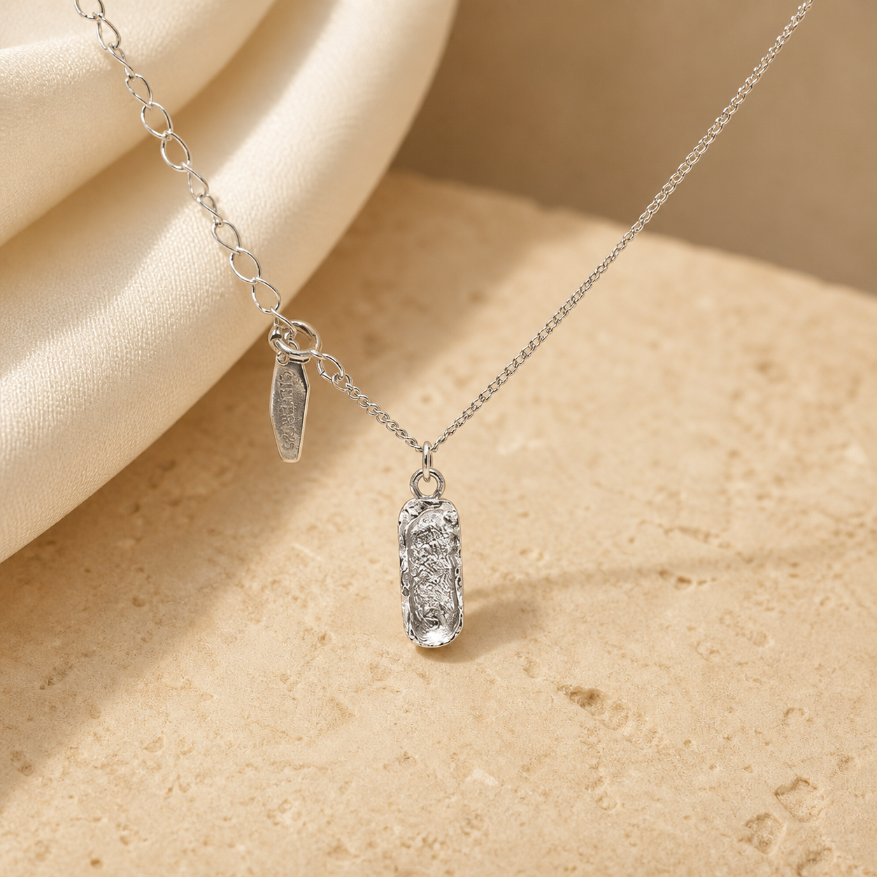 Textured silver-tone ingot pendant necklace with extension chain on warm beige stone