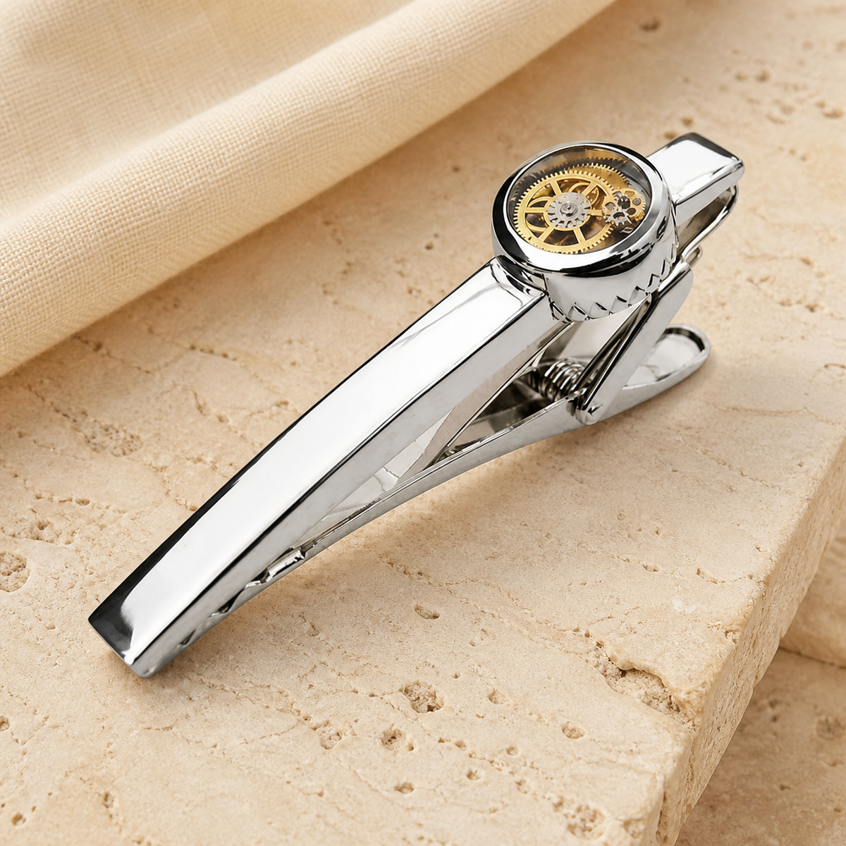 Silver tourbillon clock gear tie clip with a gold mechanism displayed on warm beige stone