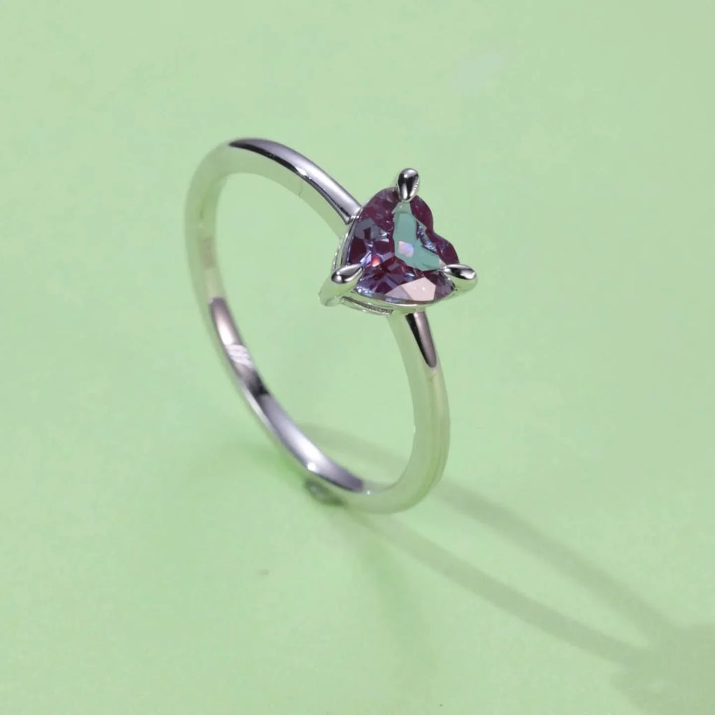 Trillion-cut Alexandrite solitaire ring, angled product view on a colored background