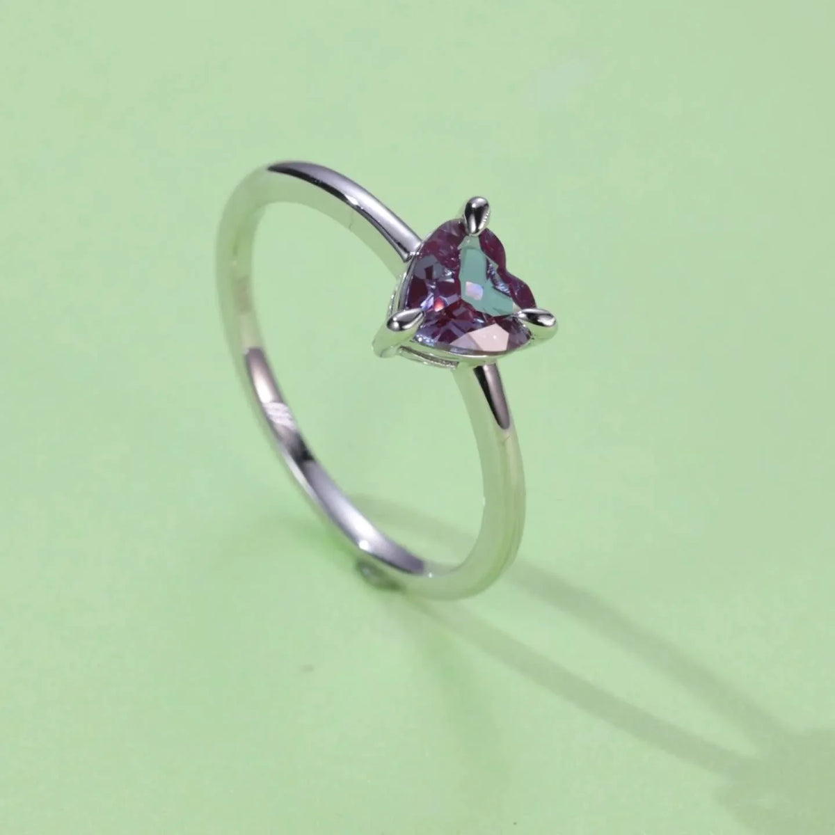 Trillion-cut Alexandrite solitaire ring, angled product view on a colored background